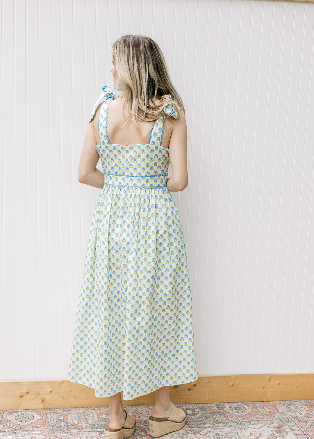 Back view of blonde model, close of white dress with blue and white print and shoulder tie.