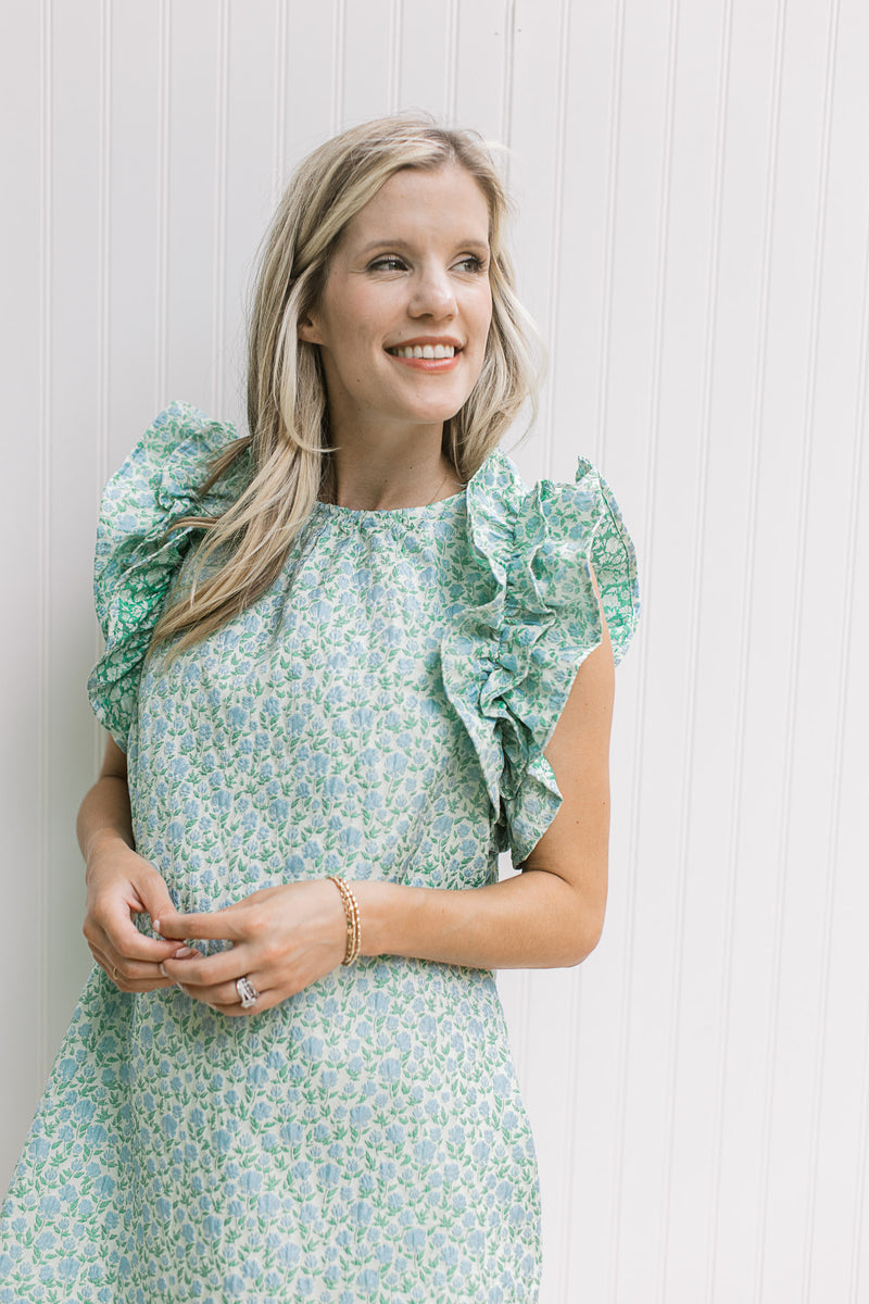 Close up of layered ruffles on a green sleeveless dress with textured material and blue floral.