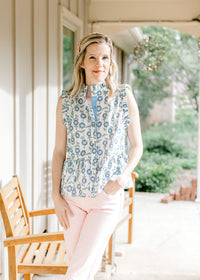 Model wearing pink pants and a white top with blue and green sunflowers, mock neck and buttons. 