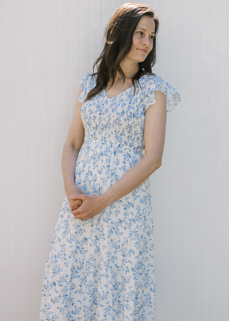 Model wearing a white with blue microfloral midi with a smocked bodice and capped sleeves. 