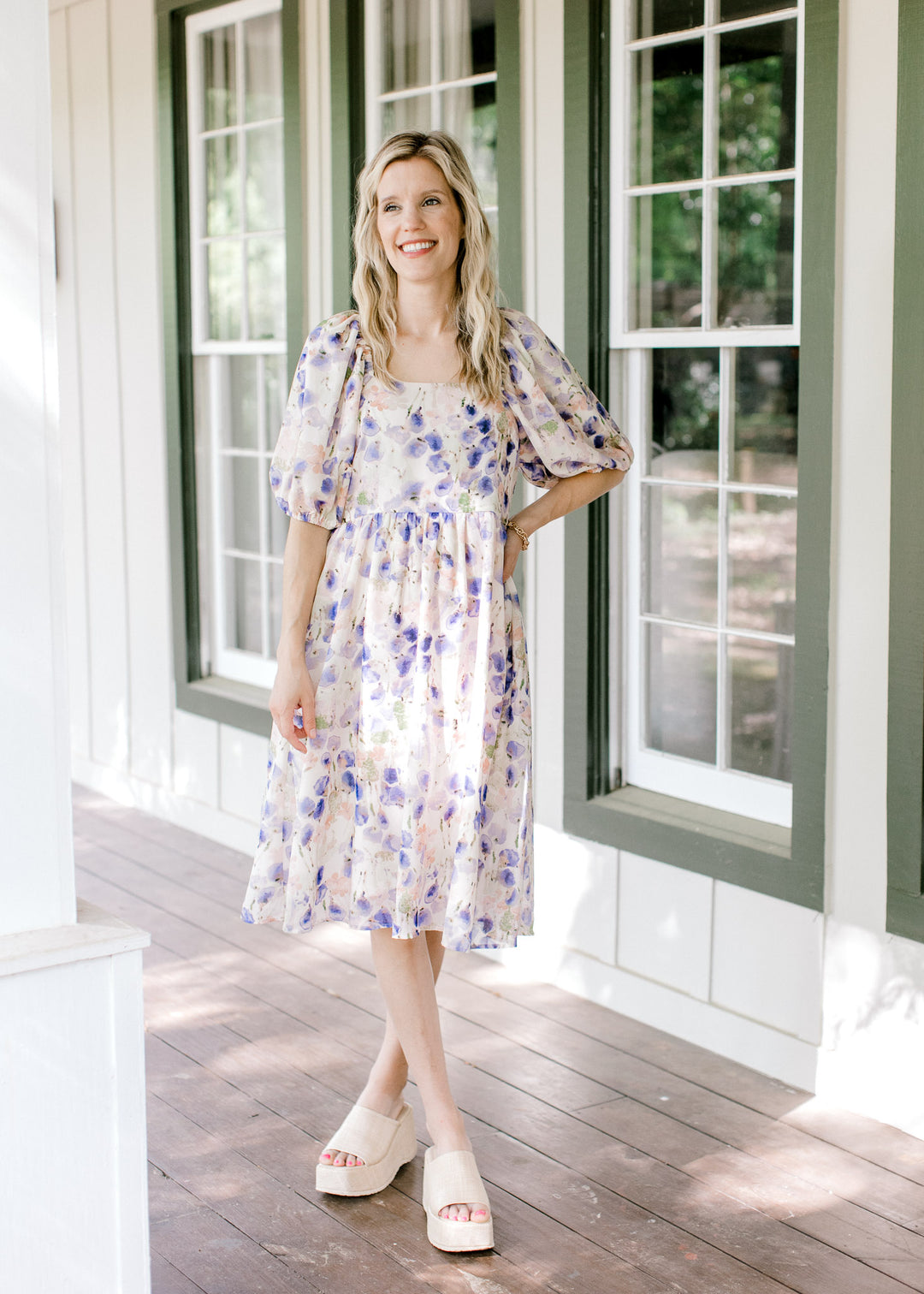 Model wearing a cream dress with violet, green and pink watercolor floral and bubble short sleeves.
