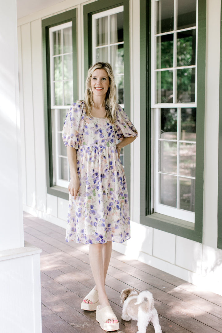 Model wearing cream dress with watercolor floral, square neck and smocked back. 