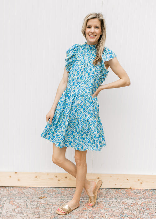 Model wearing a mint green dress with blue floral, mock neckline and ruffle cap sleeves.
