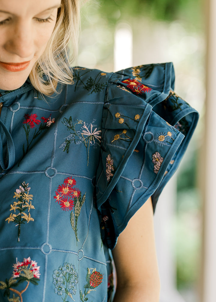 Close up of layered Capp sleeve on a blue blouse with embroidered flowers and squares. 