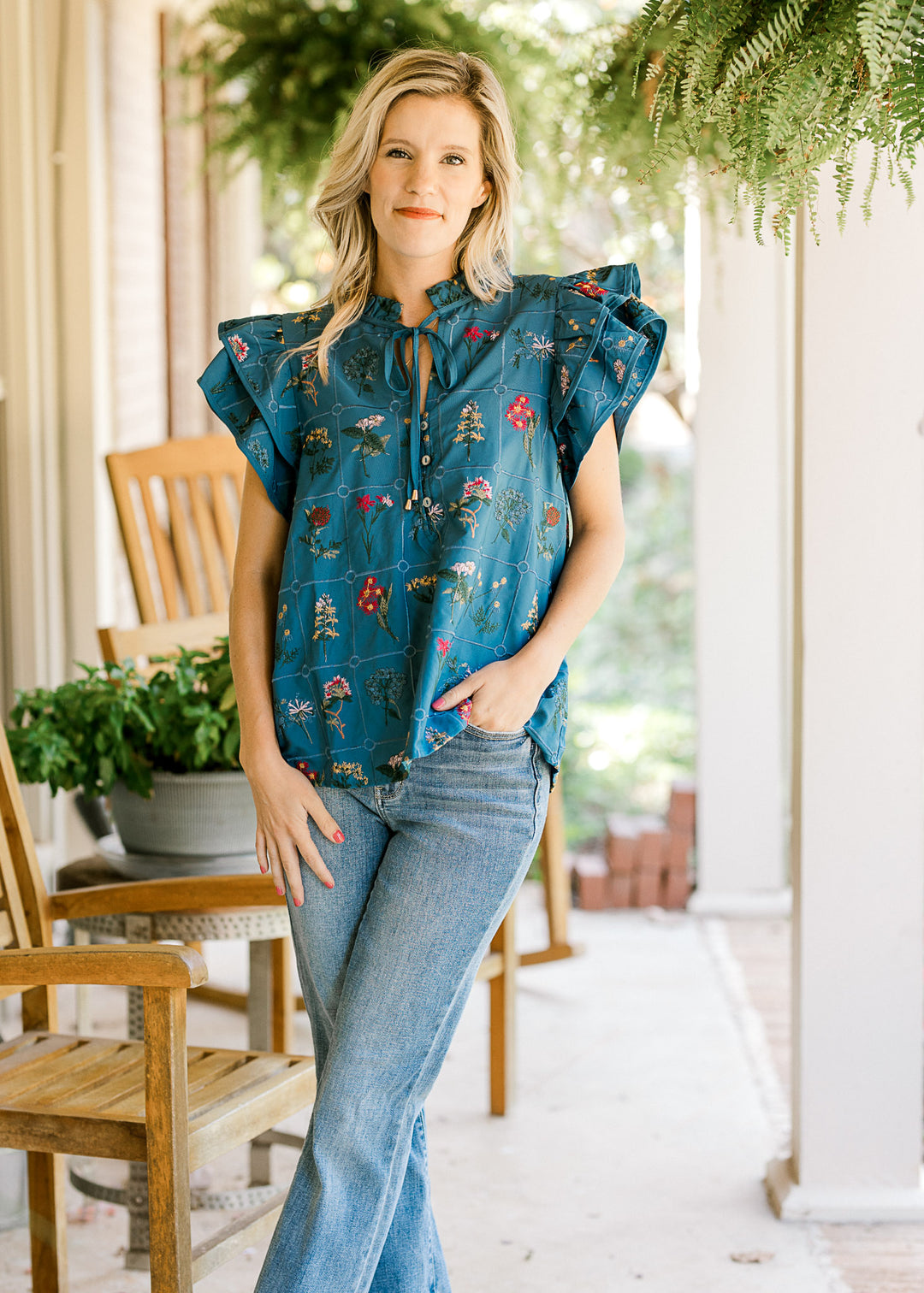 Model wearing a blue top with embroidered floral, v-neck with tie and cap sleeve. 