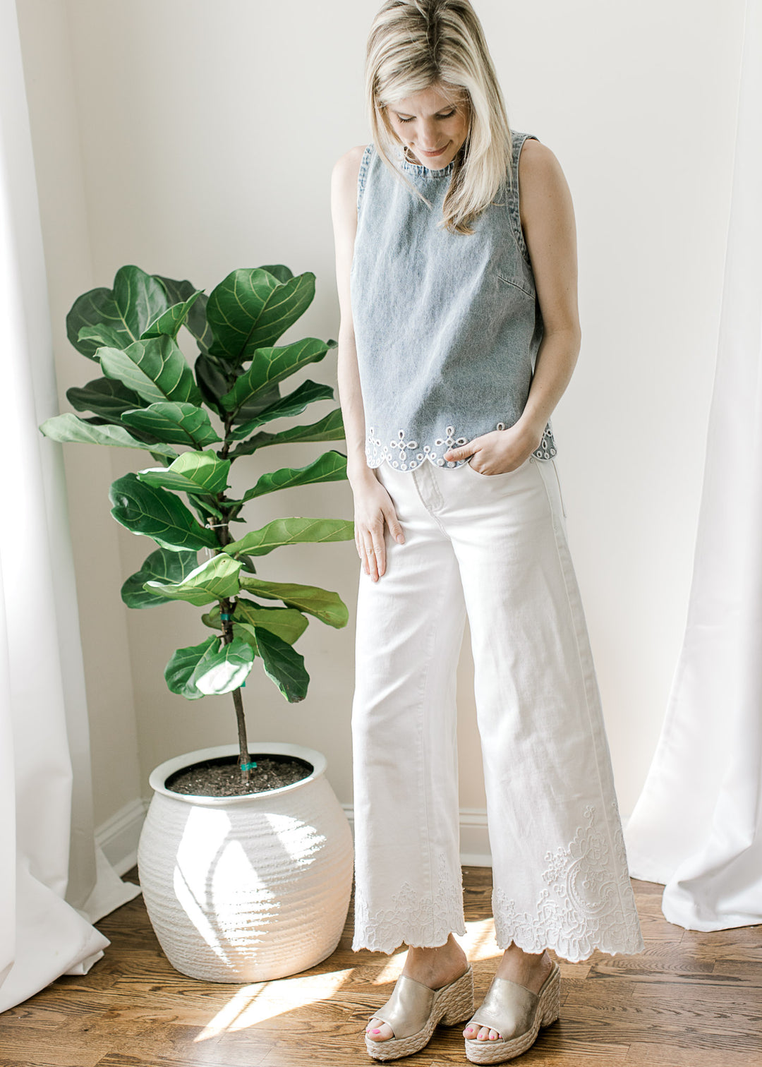 Model wearing wedges, white pants and a light wash sleeveless top with scalloped hem.