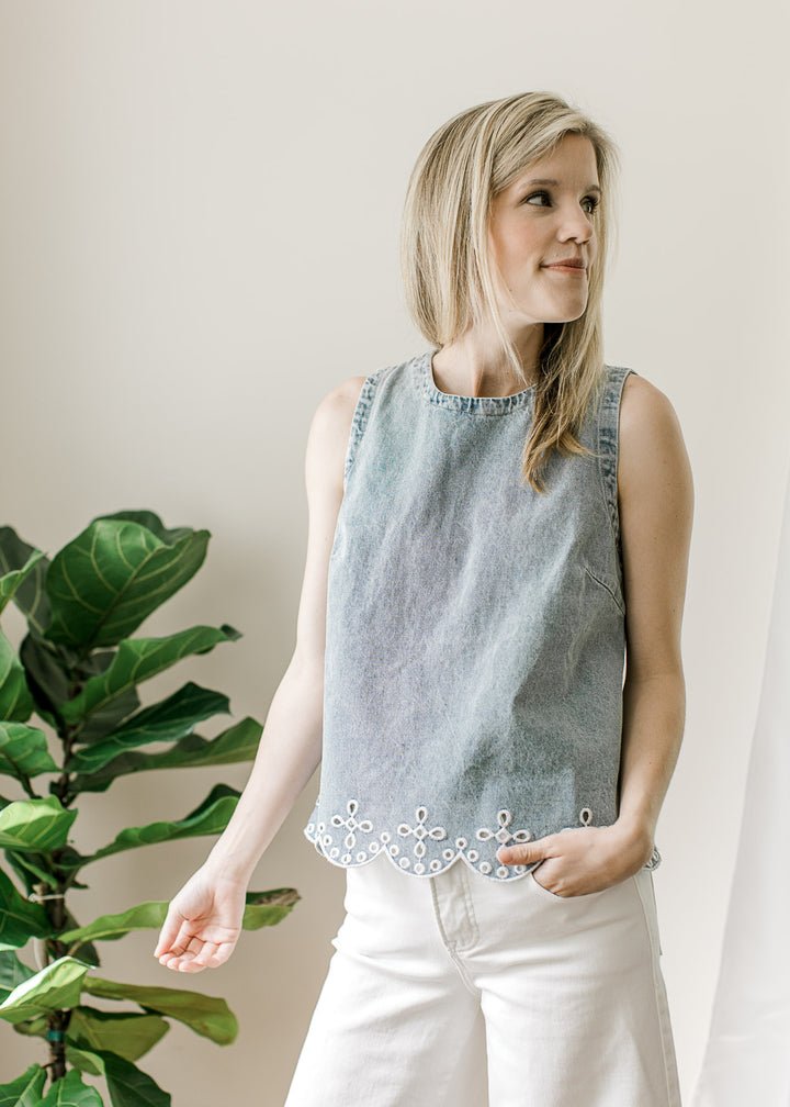 Model wearing a light wash sleeveless top with scalloped hem and embroidered eyelet at hem.