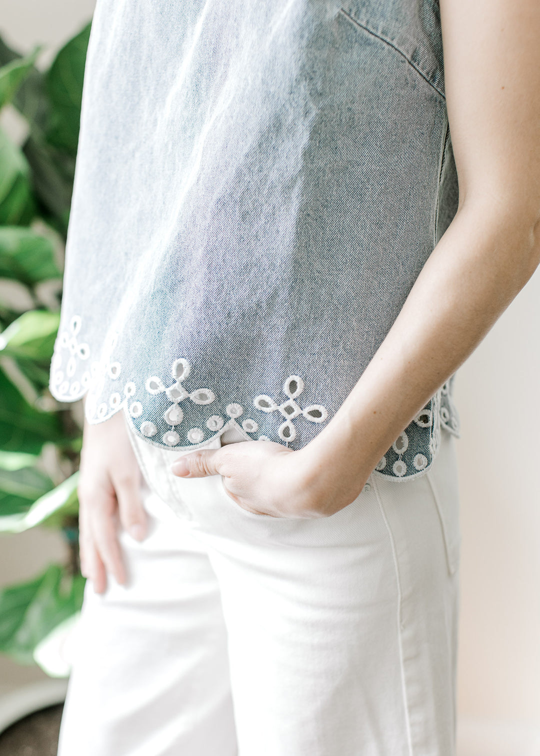 Close up of scalloped hem and embroidered eyelet hem on a light wash sleeveless top. 
