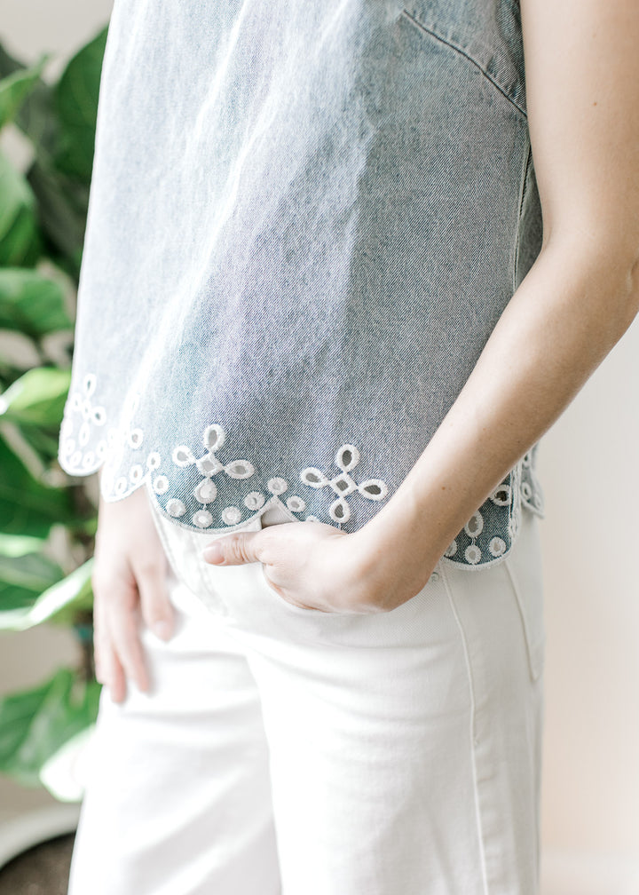 Close up of scalloped hem and embroidered eyelet hem on a light wash sleeveless top. 