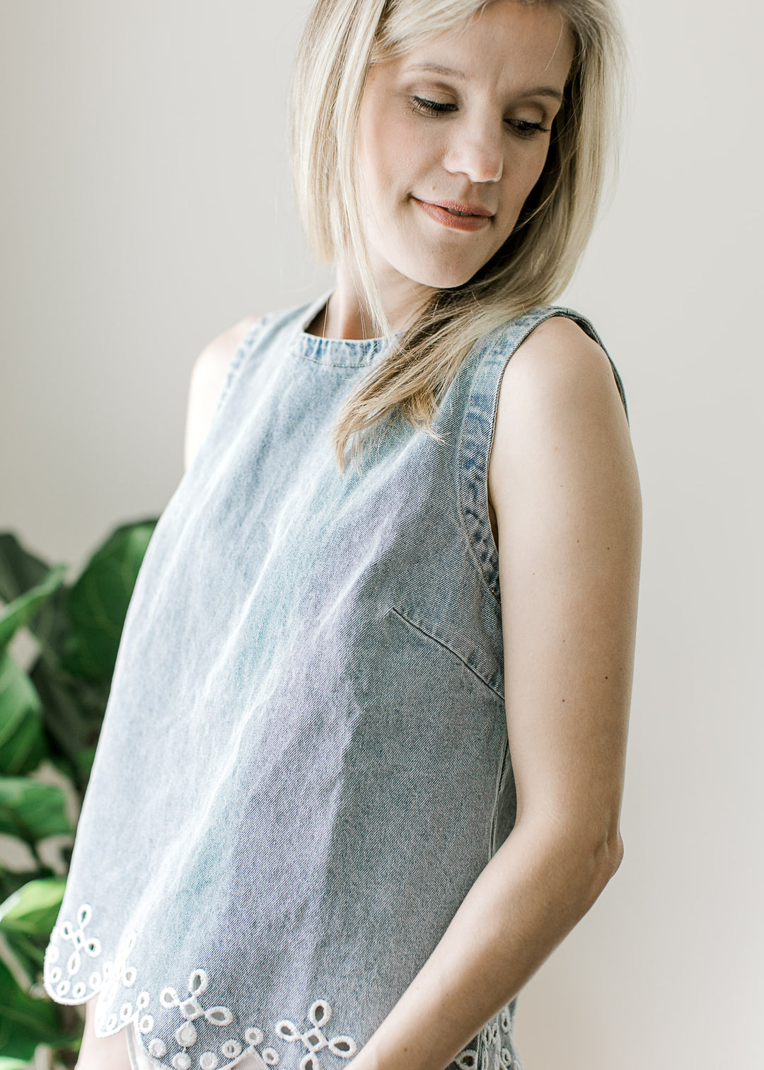 Side view of Model wearing a light wash top with scalloped hem and embroidered eyelet at hem.