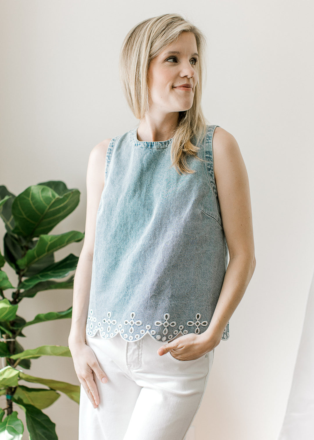 Model wearing white pants and a light wash top with scalloping and embroidered eyelet at hem.
