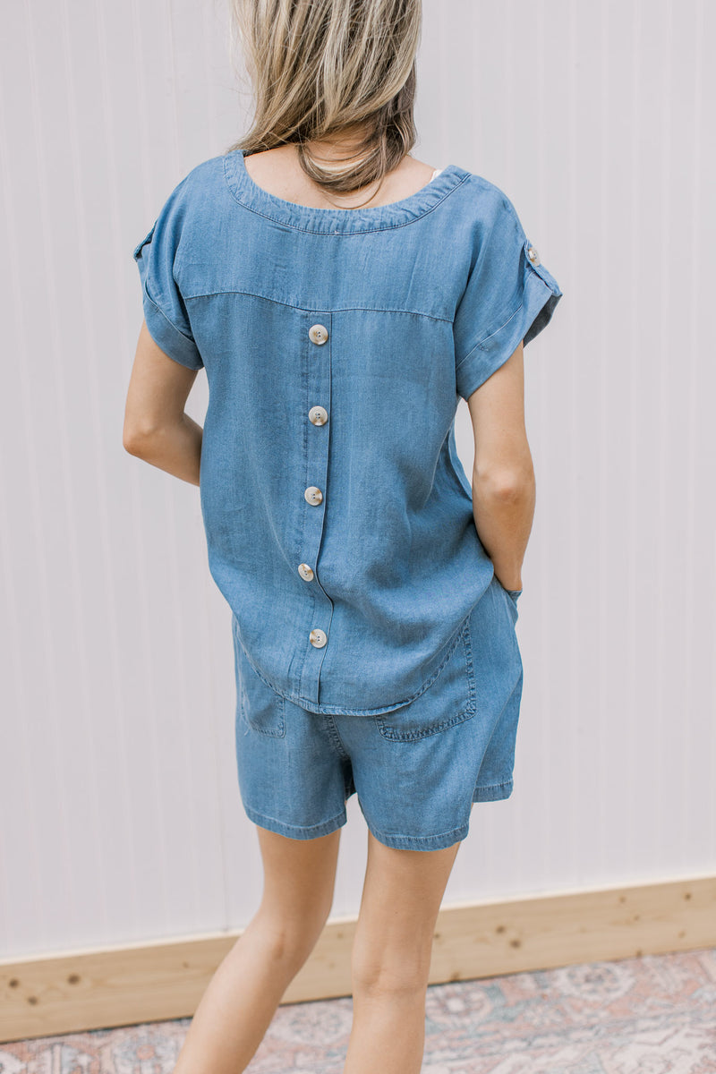 Model wearing a chambray set with elastic waist in shorts and button down back on top.