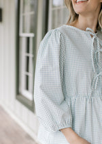 Close up of 3/4 bubble sleeves and 3 bows down the front of a blue and white checked top.