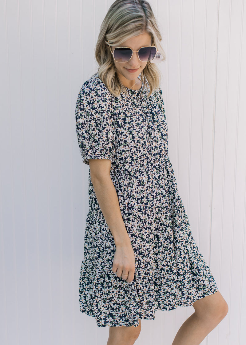 Model wearing a navy above the knee dress with a white daisy pattern and bubble short sleeves. 