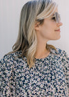 Close up view of model wearing a navy dress with a white daisy pattern and a round neckline. 