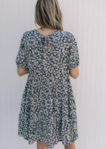 Back view of a navy above the knees dress with a white daisy pattern and a tie at the neck. 
