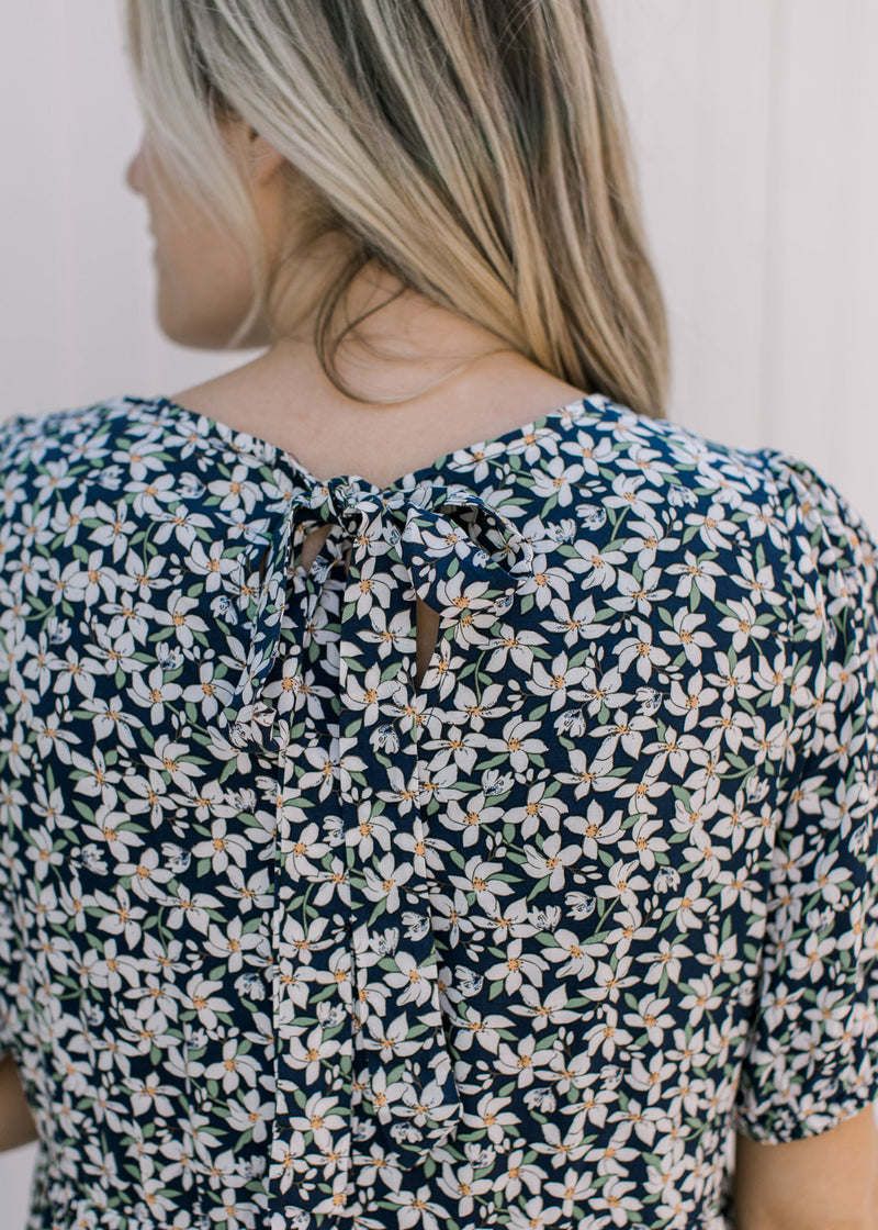 Close up view of tie closure on the back of a navy dress with a white daisy pattern. 