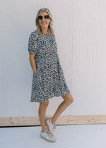 Model wearing sneakers with a navy dress with a white daisy pattern and bubble short sleeves. 