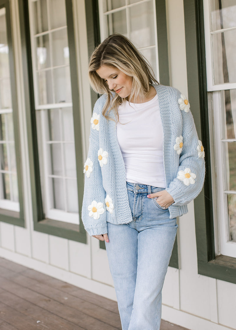 Model wearing a white top, jeans and a knit cornflower blue cardigan with long sleeves. 