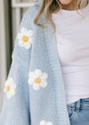 Close up of white daisies on a cornflower blue cardigan with open front and long sleeves.  