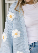 Close up of white daisies on a cornflower blue cardigan with open front and long sleeves.  