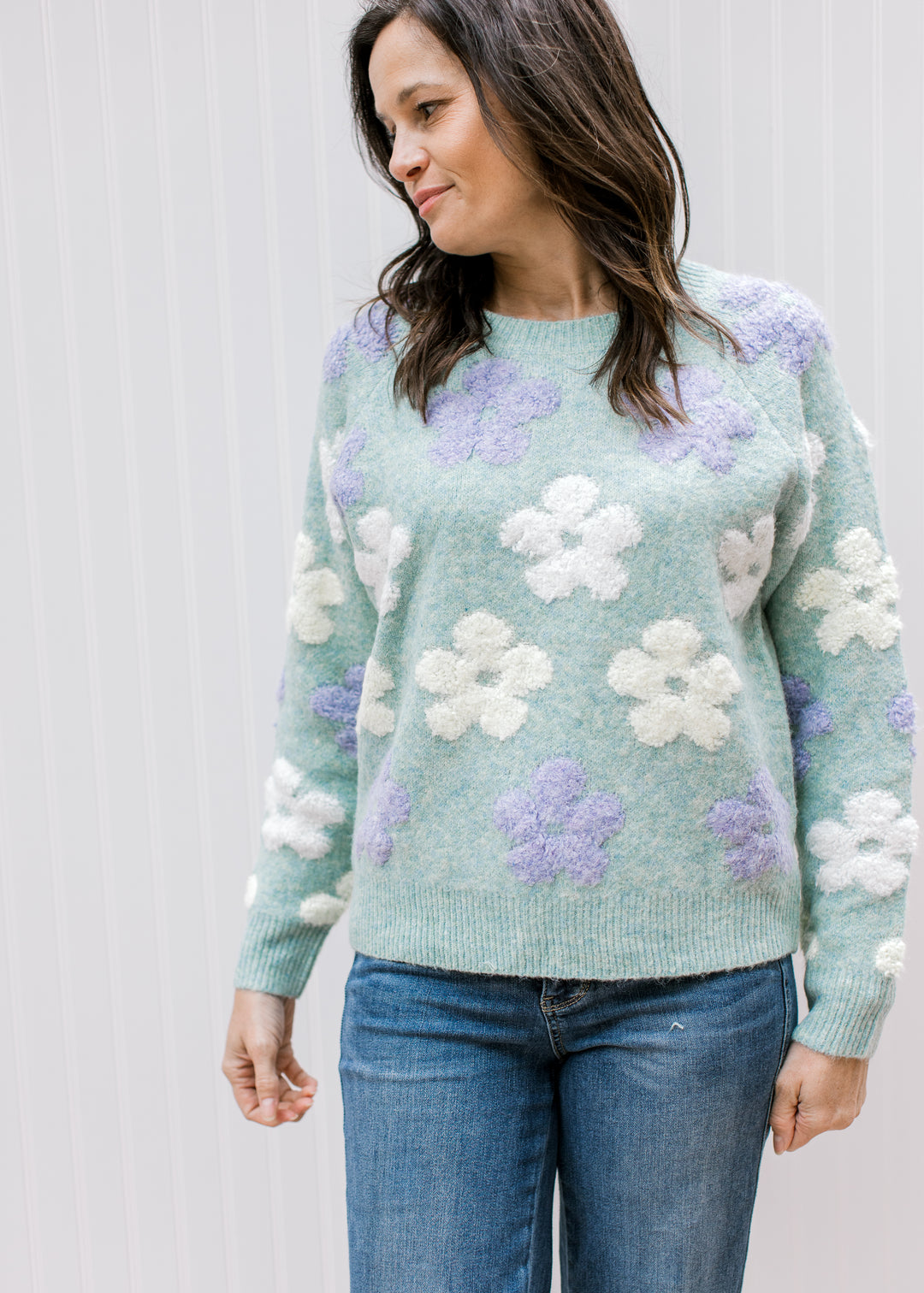 Model wearing a cozy blue-green sweater with lavender and cream textured flowers and long sleeves.
