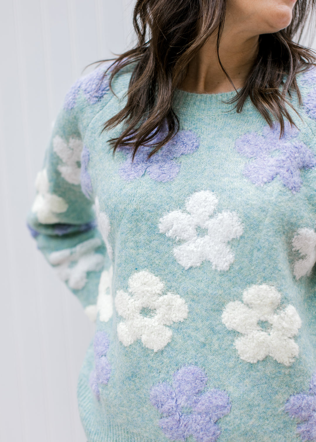 Close up on lavender and cream textured flowers on a long sleeve sweater with a round neck.