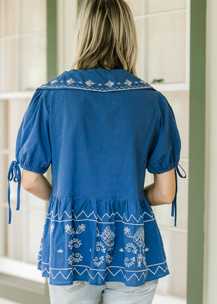 Back view of model wearing a blue babydoll top with cream floral and bubble short sleeves. 