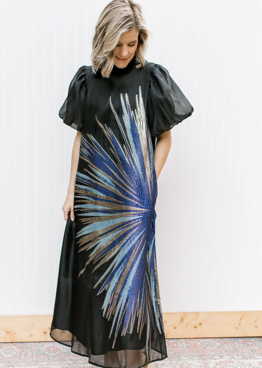 Blue Flame Dress with metallic blue and gold starburst and sheer black hem, shown with one hand in a side pocket.