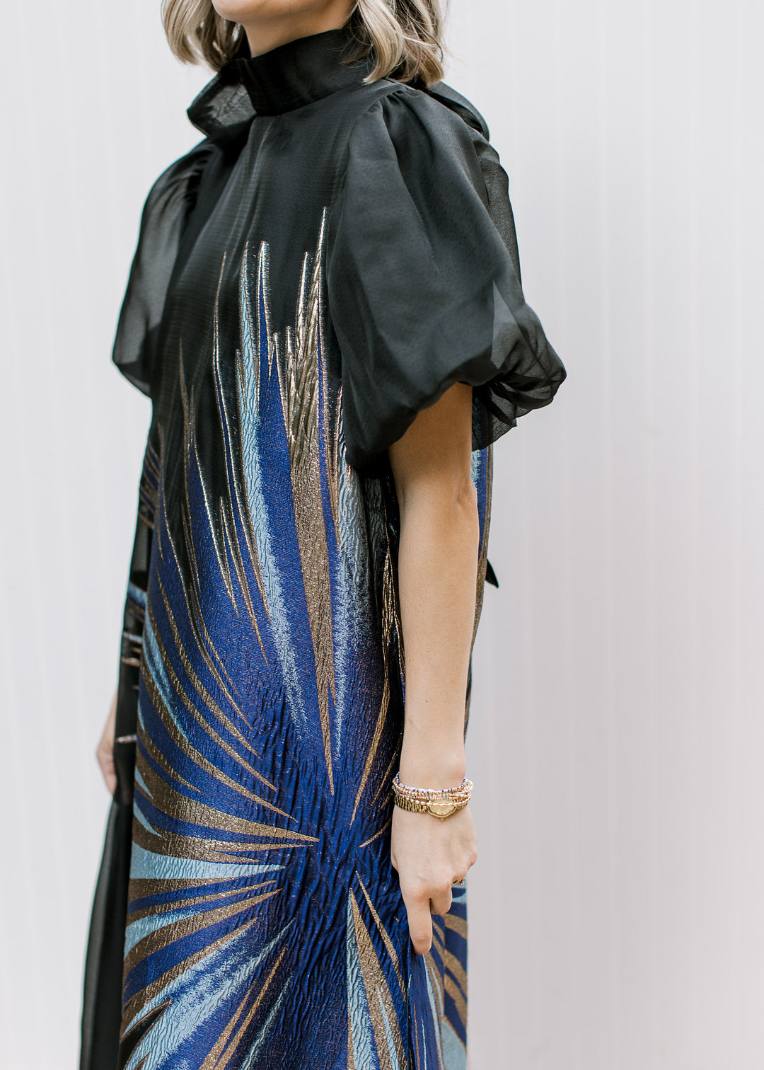 Side close-up of Blue Flame Dress with gathered sheer black bubble sleeve and metallic blue and gold starburst.