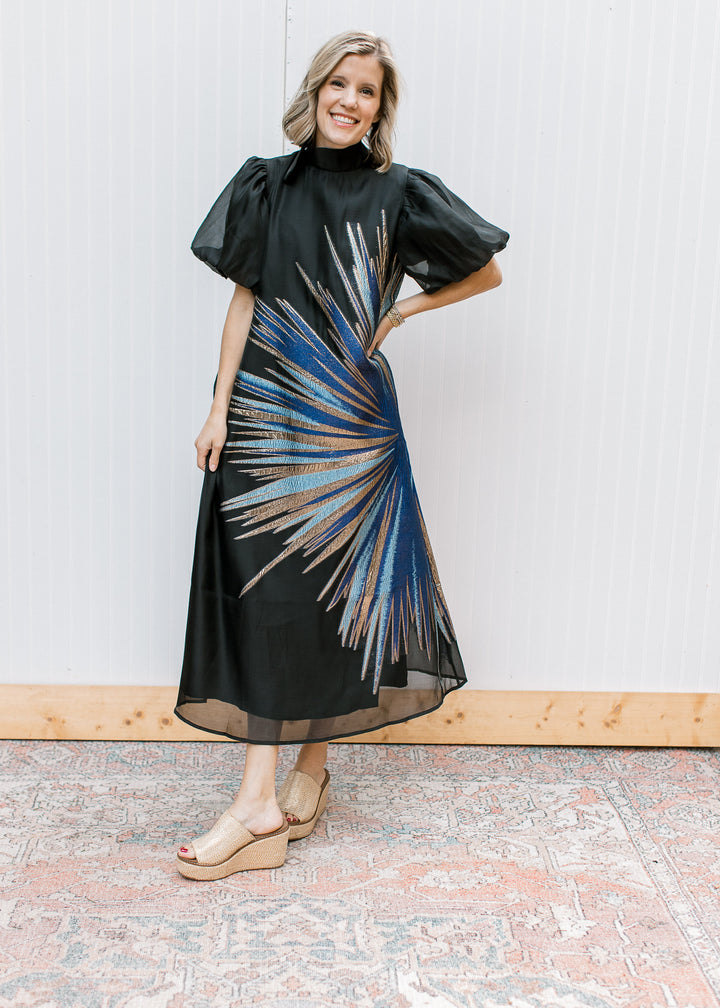 Full-length Blue Flame Dress with metallic blue and gold starburst, sheer black hem and neutral wedge sandals.