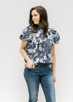 Model wearing a navy and white floral top with short puff sleeves and a round neck with a ruffle. 