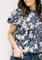 Close up view of puff sleeves and ruffle on round neck of a navy and white floral top. 