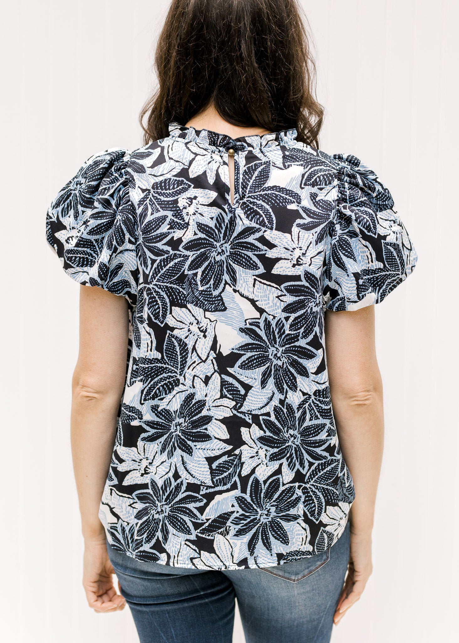 Back view of navy and white floral top with short puff sleeves and a keyhole closure. 