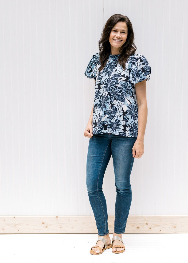 Model wearing jeans with a navy and white floral top, short puff sleeves and a ruffled round neck. 