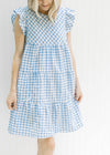 Model wearing a blue and white gingham above the knee dress with ruffle cap sleeves. 