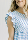 Close up of ruffle cap sleeve on a blue and white gingham dress. 