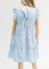 Back view of model wearing a blue and white tiered gingham dress with a tie closure. 