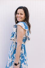 Side view of ruffle cap sleeve and two ties at the waist of a bight blue midi with cream floral. 