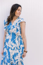 Model wearing a bright blue midi with cream floral, v-neck and ruffle cap sleeves. 