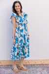 Model wearing a bright blue midi with cream floral, ruffle cap sleeves and two side waist ties. 