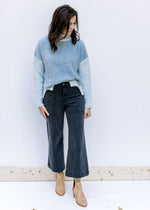 Model wearing jeans, mules and a blue and gray colorblock sweater with long sleeves and split sides.