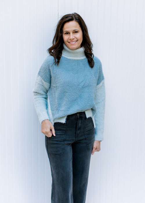 Model wearing a blue and gray colorblock turtleneck sweater with long sleeves and split sides. 