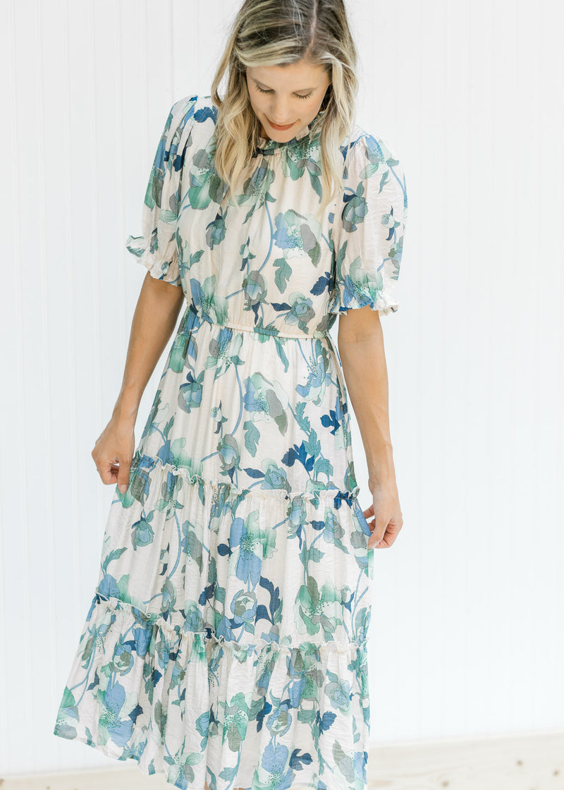 Model wearing a cream midi dress with a blue and green floral pattern and short bubble sleeves.
