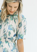 Close up view of bubble short sleeves and elastic waist on a cream dress with blue and green floral 