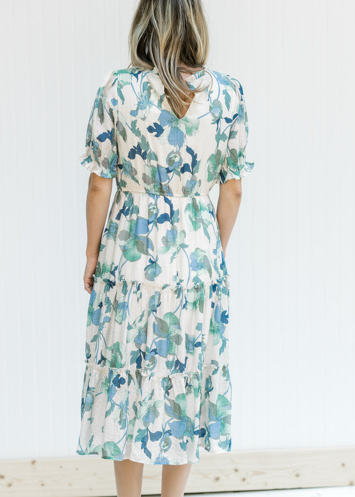 Back view of Model wearing a cream midi dress with a blue and green floral and short sleeves.