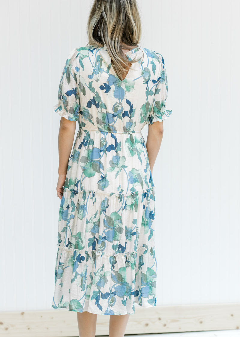 Back view of Model wearing a cream midi dress with a blue and green floral and short sleeves.