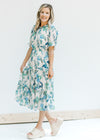 Model wearing heels with a cream midi dress with a blue and green floral pattern and short sleeves.