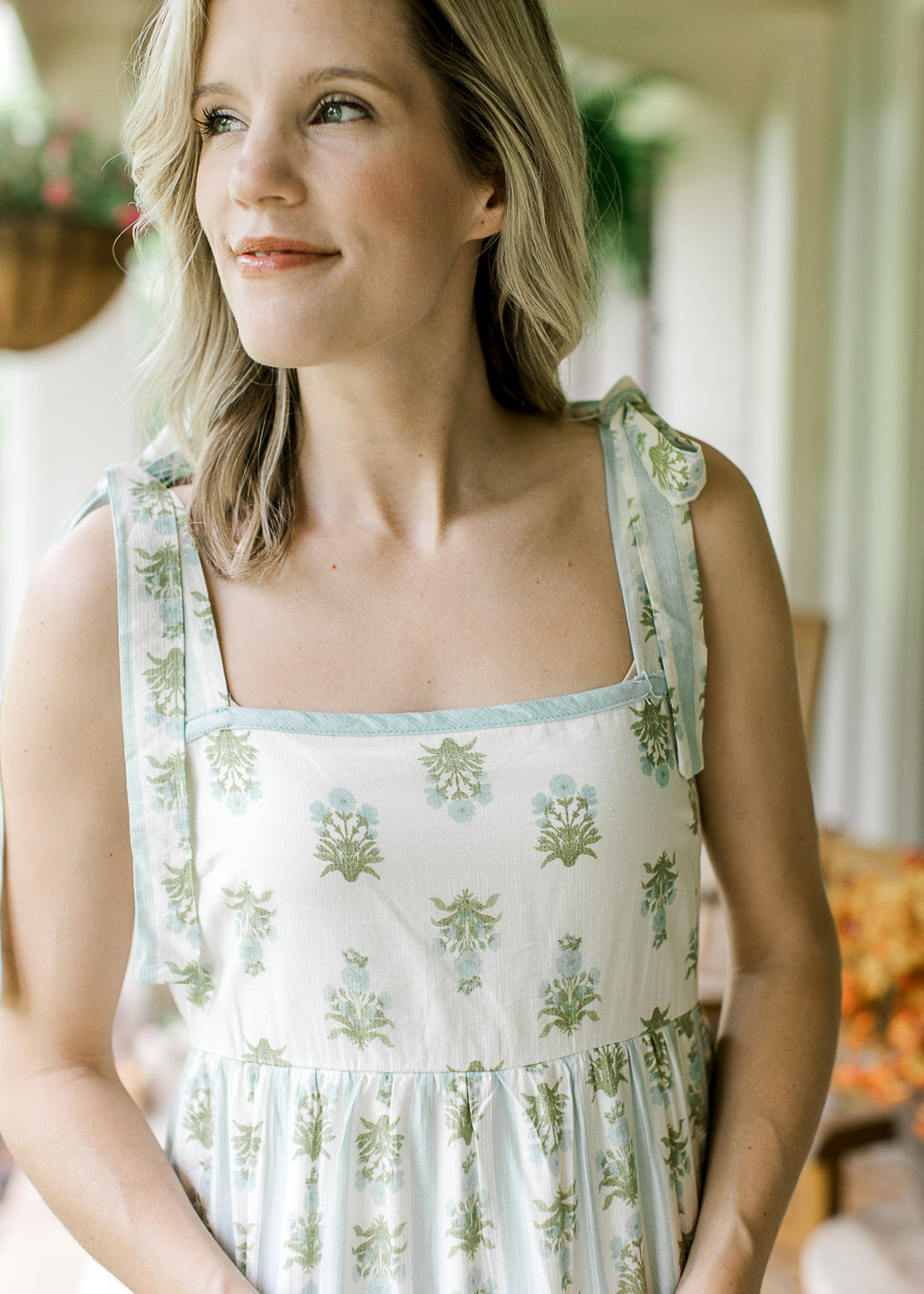 Close up of square neck and tie straps on a cream midi with blue and green striped floral. 