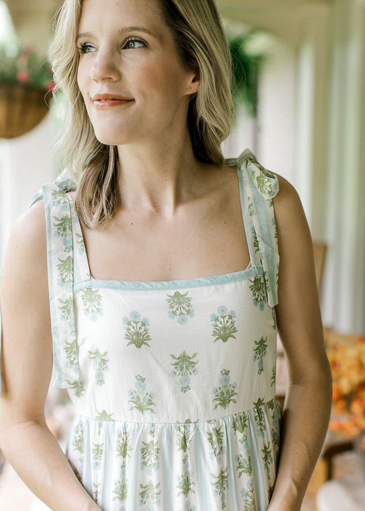 Close up of square neck and tie straps on a cream midi with blue and green striped floral. 